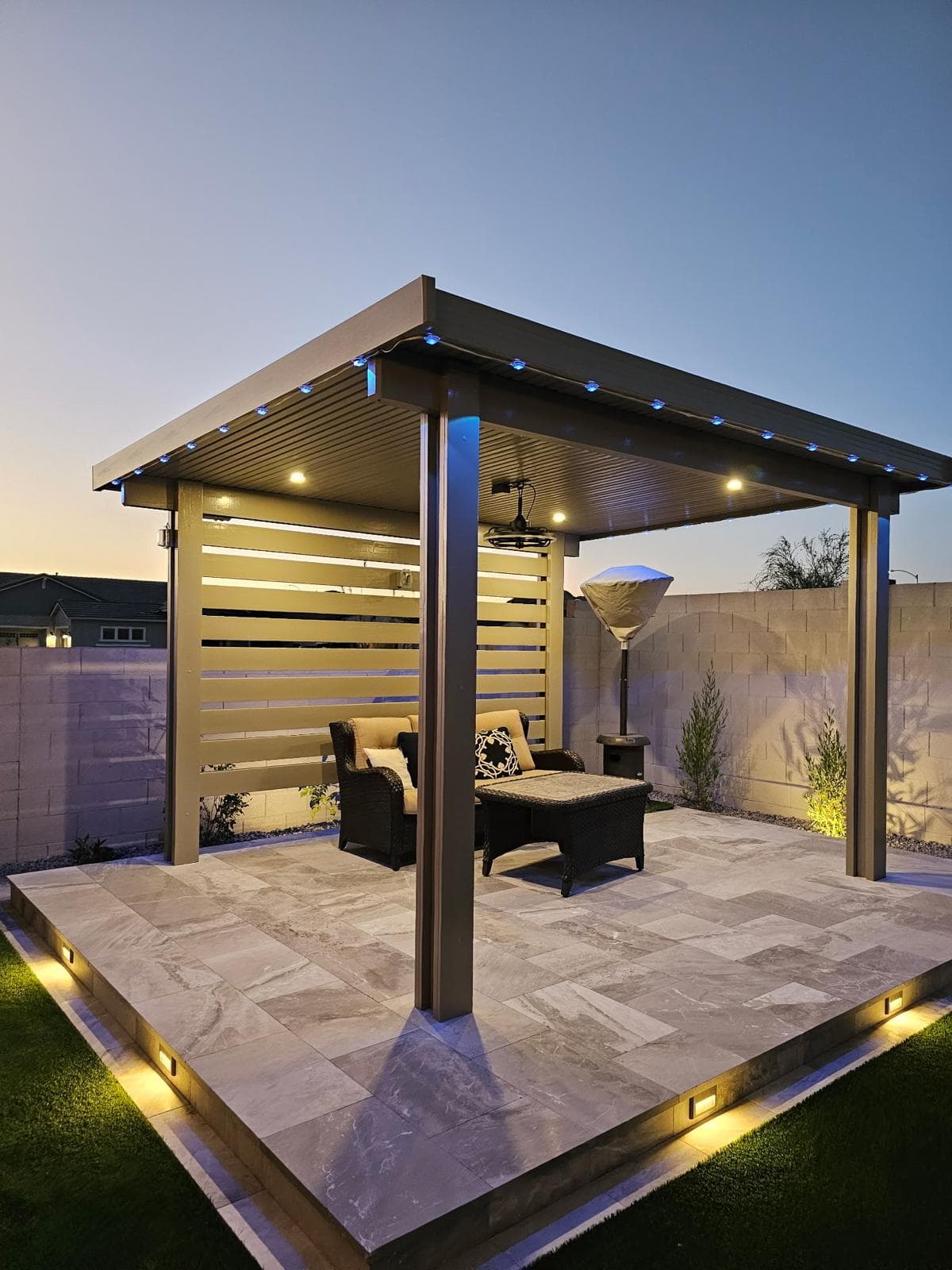 A louvred pergola over travertine paving, with a turf and stone paver grid leading to a putting green