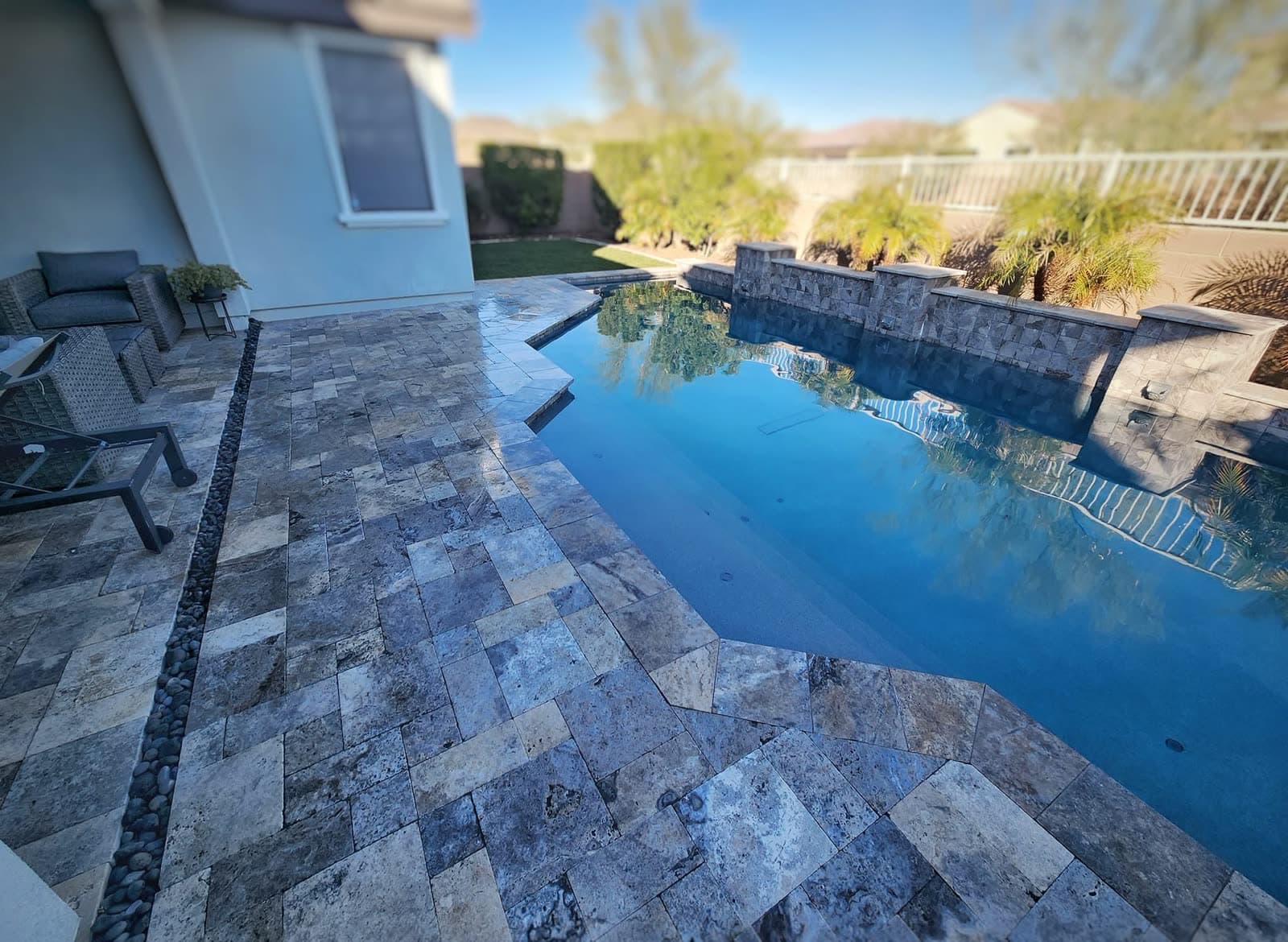 Silver travertine decking around a pool with a stacked-stone water wall