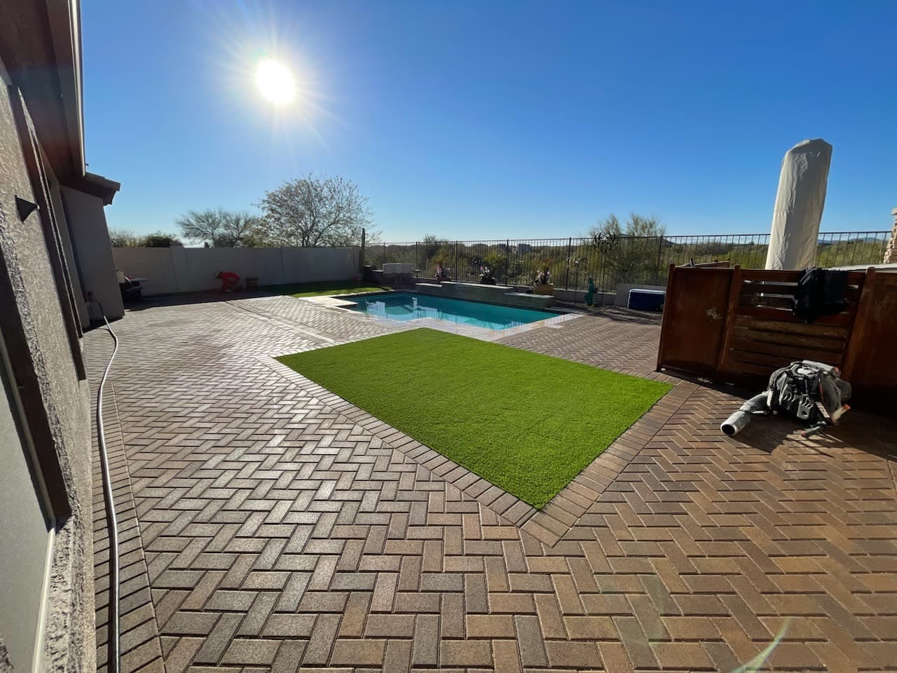 Herringbone pavers wrapping a pool with a turf panel and open desert views